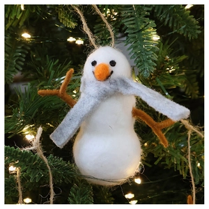 Close-up of handmade wool felt snowman ornament hanging on a Christmas tree with warm lights