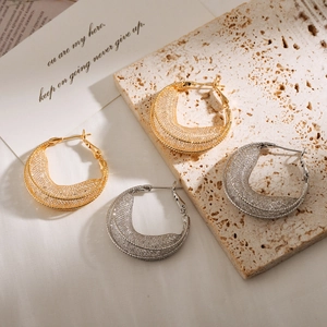 Detail of woven mesh hollow earrings in gold and silver finish on artistic beige stone