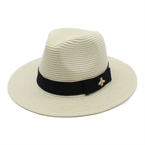Detailed macro view of cream straw fedora with black ribbon and gold bee accent