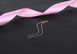 Macro detail of elegant rose gold tassel earrings with fine chain on black background