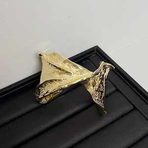 Macro detail showing the golden irregular wrinkled texture on a wide metallic cuff bracelet