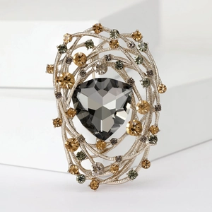 Macro shot of silver bird nest brooch with a grey triangular crystal and olive gems
