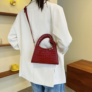 Detail of burgundy crocodile pattern handbag with unique heart-shaped cutout handle