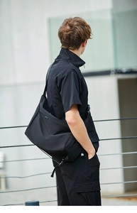Modello maschile che indossa una grande borsa a tracolla nera in un contesto urbano moderno