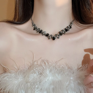 Detail of silver V-shaped necklace with black teardrop pendant and white crystals on neck