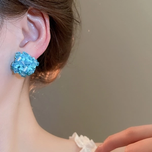 Detailaufnahme blauer Kristall-Ohrstecker beim Tragen mit warmem Lichteffekt