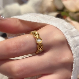 Detail of open gold ring featuring geometric hollow coins and opal stone on finger