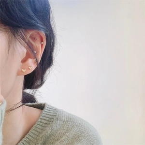 Detailed view of minimalist gold heart stud earrings and tiny cartilage studs on ear