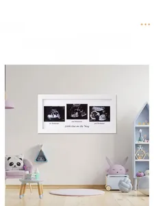 Three-section white wooden baby sonogram frame displaying pregnancy milestones on a shelf