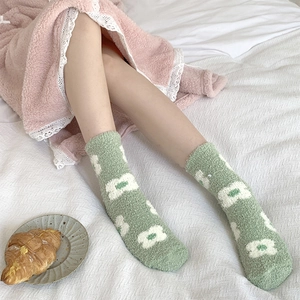 Close-up of soft green coral fleece socks with floral patterns on white bedding