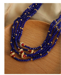 Close-up of multilayer beaded necklace with blue crystals and red charms on wood