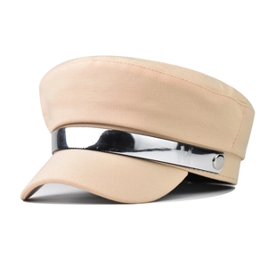 Detail of beige baker boy hat featuring a silver metallic M-embossed band and buttons