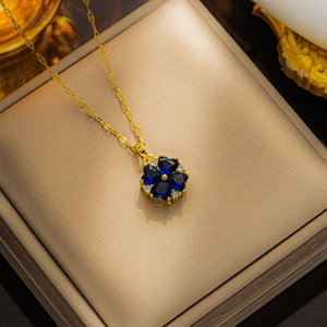 Gold four-leaf clover necklace with blue heart zircon stones on a jewelry box