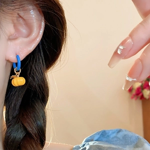 Close-up of model wearing blue hoop earrings with yellow pumpkin charm details