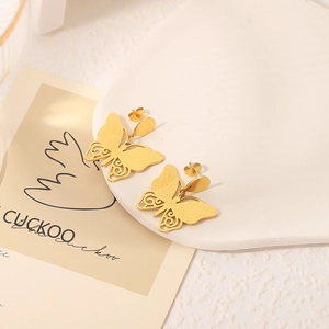 Élégantes boucles d'oreilles papillon dorées ajourées sur un plateau blanc décoré