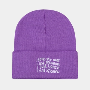 Detailed close-up of purple ribbed knit beanie featuring white embroidered slogans