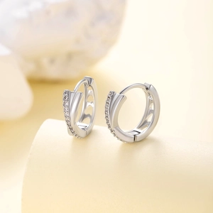Elegant silver-colored crisscross hoop earrings with inlaid zircon on a beige pedestal
