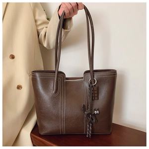 Detail of dark brown tote bag with cat charm and white contrast stitching on leather