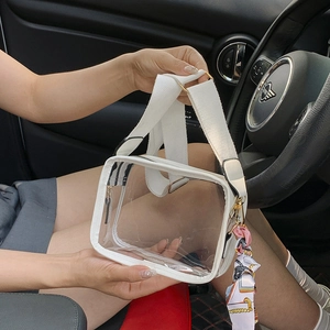 Clear PVC crossbody bag with wide white strap and floral scarf on car interior background