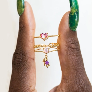 Detail of gold rings set featuring pink heart stones and a purple bear charm pendant