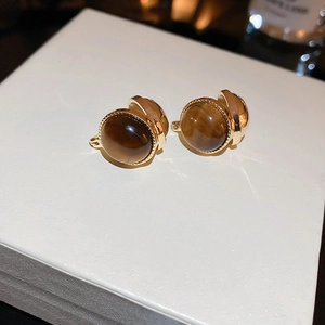 Macro shot of tiger eye clip-on earrings with gold textured edges on a white box