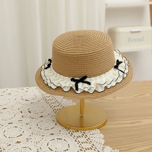 Detail of straw hat with white ruffled trim and black bows on a gold metal stand