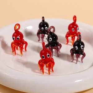 Close-up of six handmade mini octopus glass charms in red and dark purple for jewelry making