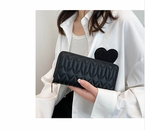 Detail of black quilted faux leather wallet with gold zipper held by a person