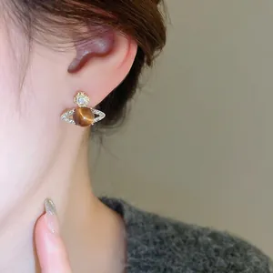 Elegant gold planet earrings with brown cat-eye stone and rhinestones worn on ear