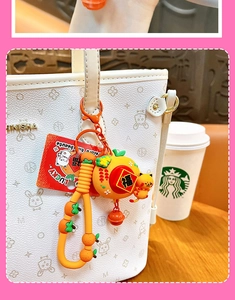 Close-up of a lucky cat and orange-shaped bag charm on a white handbag