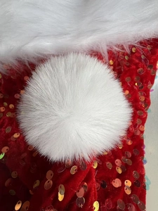 Macro detail of plush white pom-pom and sparkling red sequins on a Christmas hat
