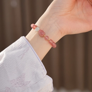Detailed close-up of pink strawberry quartz bracelet with a cute cat charm on wrist