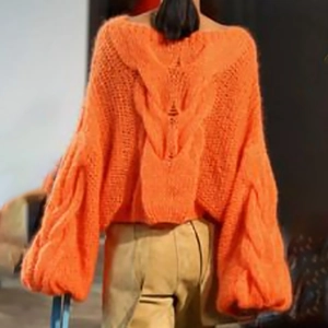 Detail of chunky cable knit texture on a vibrant orange oversized sweater from the back