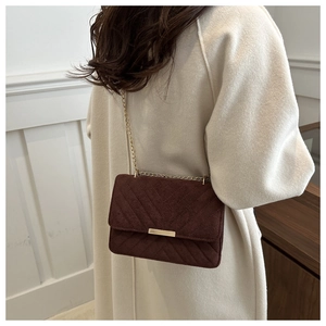 Detail of burgundy suede shoulder bag with V-shaped quilting and gold chain strap