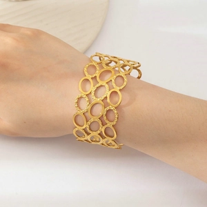 Detailed close-up of wide hollow gold titanium steel bracelet with textured oval rings