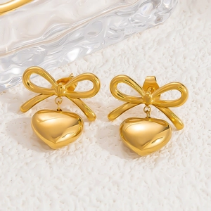 Detail shot of 18k gold plated bow and heart drop earrings on a glass texture