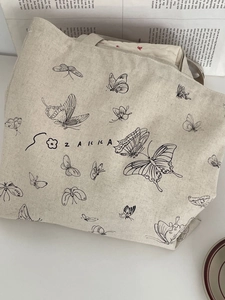 Dettaglio della stampa a farfalla e del testo Zakka su borsa tote in tela beige minimalista