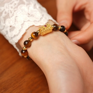 Detail of tiger eye bead bracelet with gold metal charm on a warm wooden background