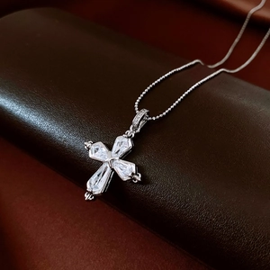 Macro view of a silver cross pendant featuring four pear-cut zircons on a beaded chain