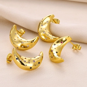 Macro shot of gold moon earrings with colorful cubic zirconia on textured fabric