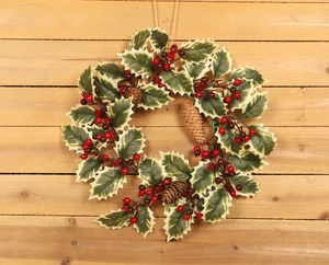 Detail view of a Christmas wreath with holly leaves, pine cones, and red berries on wood