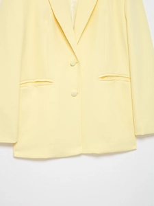 Detail of light yellow blazer with notched lapels and matching buttons on textured fabric