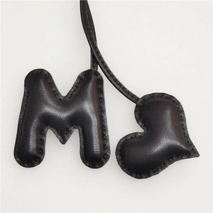Detailed close-up of hand-stitched black leather letter M and heart shape bag charms