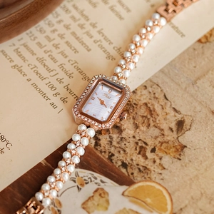 Close-up of elegant gold rectangular watch with pearl strap and crystal bezel on vintage paper