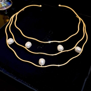 Detail view of a multi-layer gold wave choker necklace with white baroque pearls