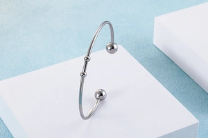 Macro detail of silver stainless steel open bangle with bead accents on white pedestal