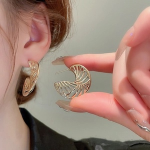 Macro detail of gold plated fan-shaped hollow earrings on ear for size reference