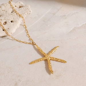 Détail d'un collier pendentif étoile de mer plaqué or 18 carats sur marbre beige