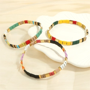 Close-up of three colorful beaded bracelets on shell dish with satin background