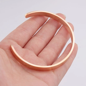 Detail of rose gold open cuff bracelet with brushed metal texture held by hand